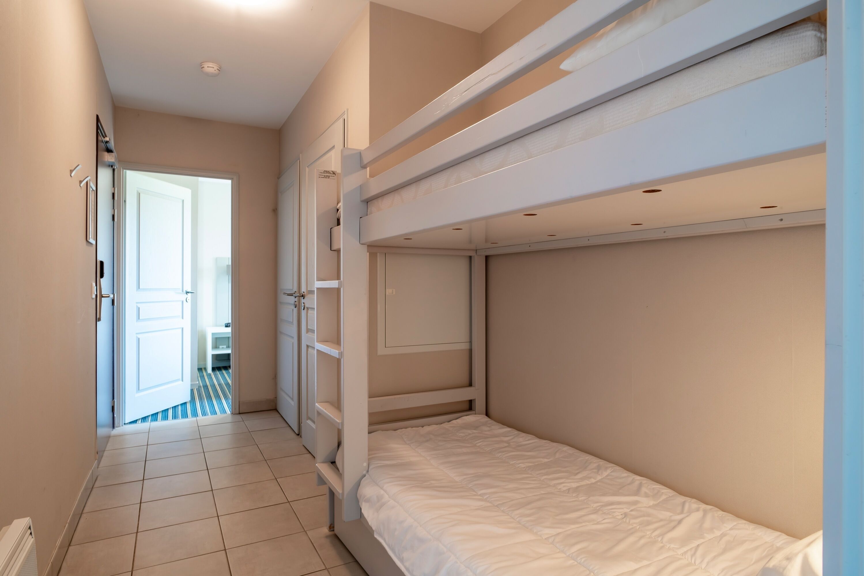 A room with bunk beds, a door leading to another room, and a tiled floor.