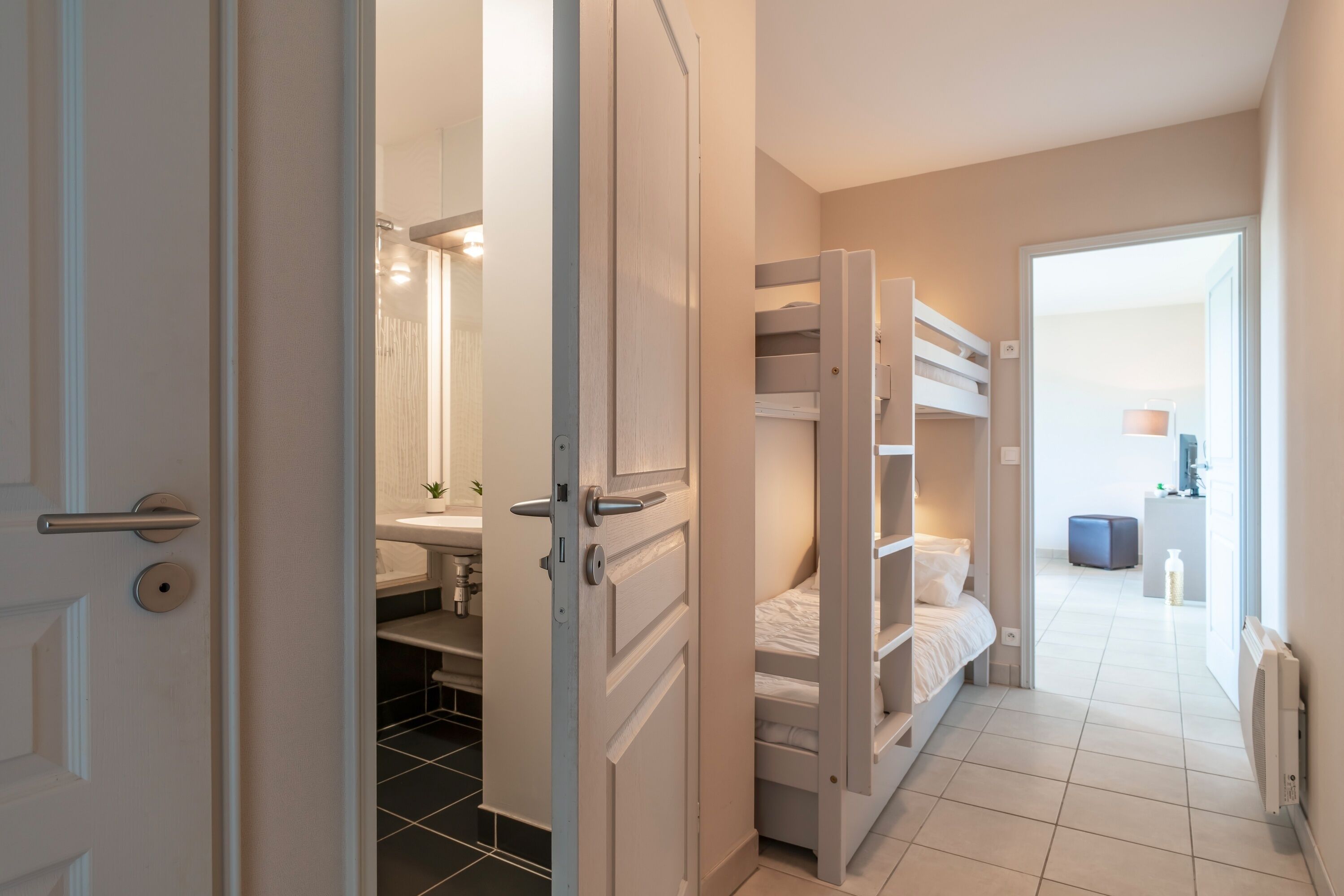 A bedroom with a bunk bed, a bedside table, and a bathroom with a sink and mirror.