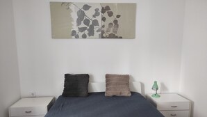 Ein Schlafzimmer mit einem Bett, zwei Kissen, einem Nachttisch mit Lampe und einem Wandbild.