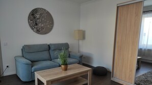 Ein modernes Wohnzimmer mit einem grauen Sofa, einem Holztisch, einer Topfpflanze, einem runden Wandbild, einer Stehlampe und einem großen Spiegel.