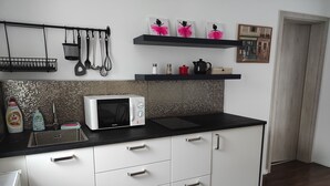 Eine moderne Küche mit weißen Schränken, einer schwarzen Arbeitsplatte und einer Mikrowelle. Es hängen Besteck und ein Regal mit Dekorationsobjekten an der Wand.