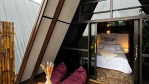 A modern loft bedroom with a sloped ceiling, a wooden table with a vase, and a view of the outdoors. - Chalet Bromo lounge & lodge (Kedungredjo)