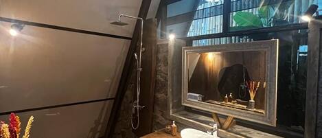 A modern bathroom with a stone floor, a large mirror, a sink, and a shower.