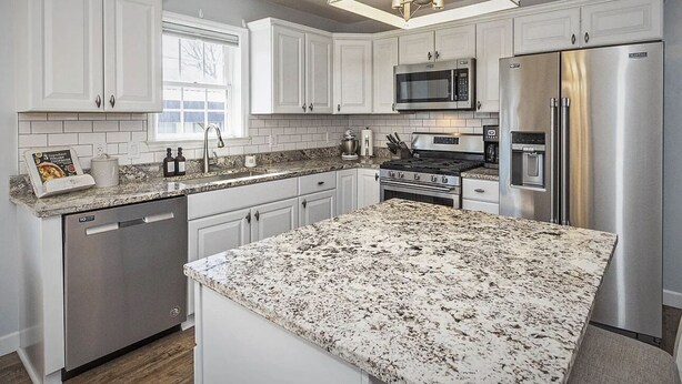 A modern kitchen with white cabinetry, stainless steel appliances, and a granite countertop.