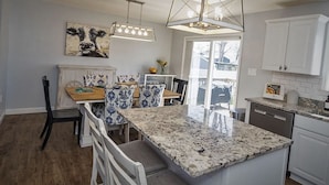 A modern kitchen with a granite island, white cabinetry, and pendant lighting.