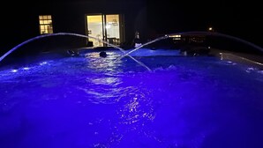 A nighttime view of a swimming pool with blue lighting, a building with a lit entrance, and a clear sky.