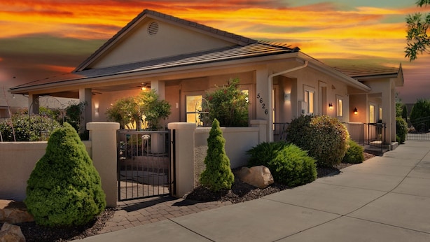 A two-story house with a covered porch, a gated entrance, and a well-maintained front yard with shrubs and a small tree. - Hole in One! Luxury Home Near Golf Course, Airport, Embry Riddle (Prescott)