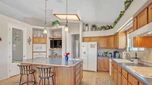A kitchen with wooden cabinets, a central island with stools, a microwave, and a refrigerator. - Hole in One! Luxury Home Near Golf Course, Airport, Embry Riddle (Prescott)