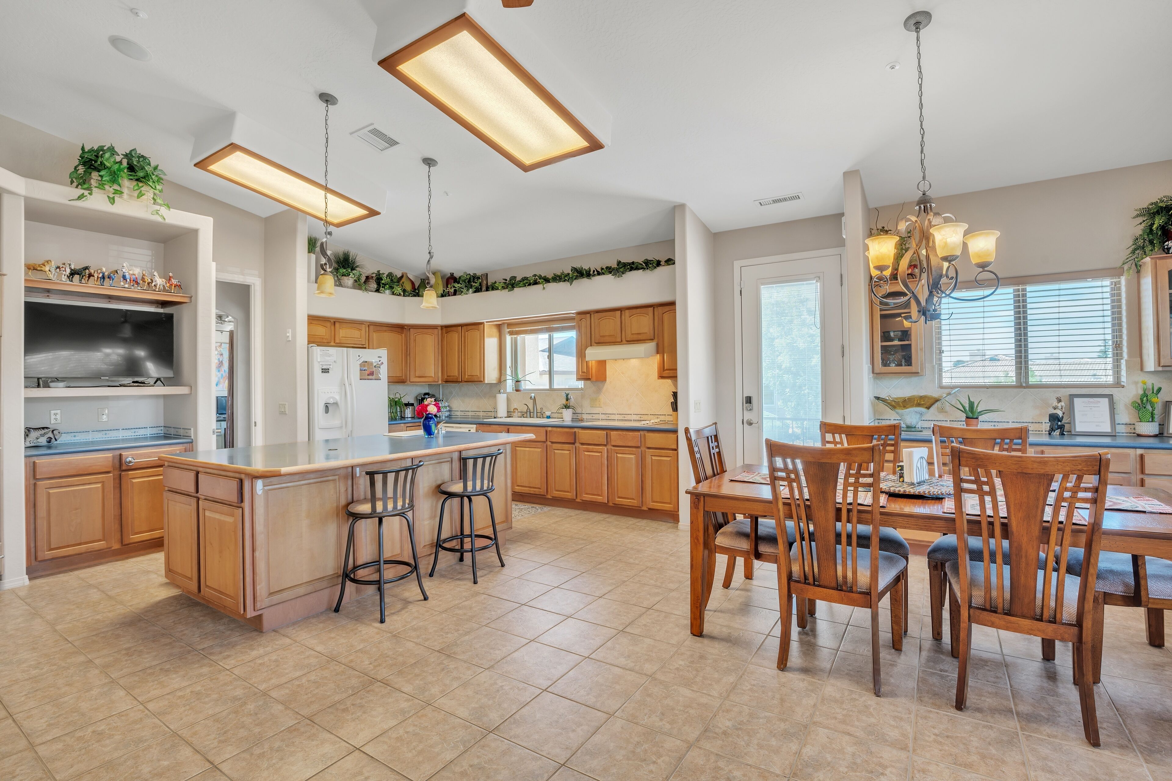 A spacious kitchen with wooden cabinets, a large island with bar stools, and pendant lighting.