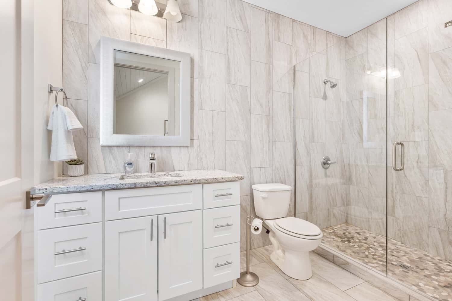 A modern bathroom with a marble backsplash, a large mirror, a toilet, and a shower enclosure.