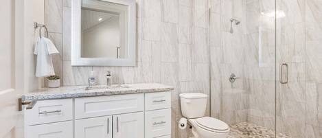 A modern bathroom with a marble backsplash, a large mirror, a toilet, and a shower enclosure.