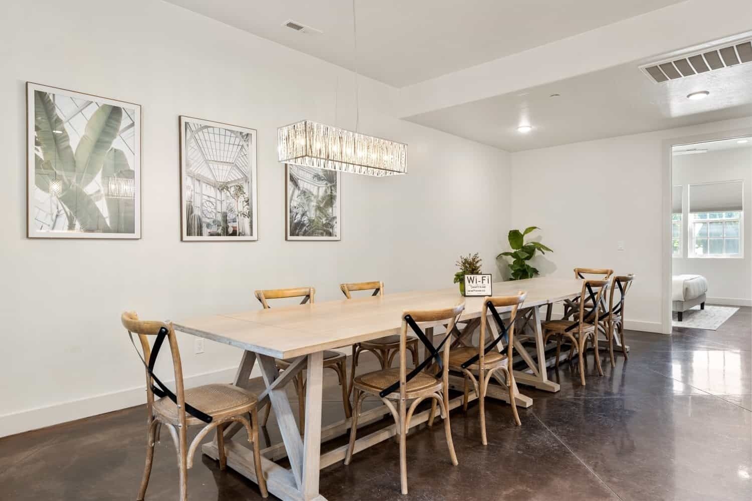 A modern dining area with a long wooden table and chairs, framed artwork on the walls, and a sign indicating Wi-Fi availability.
