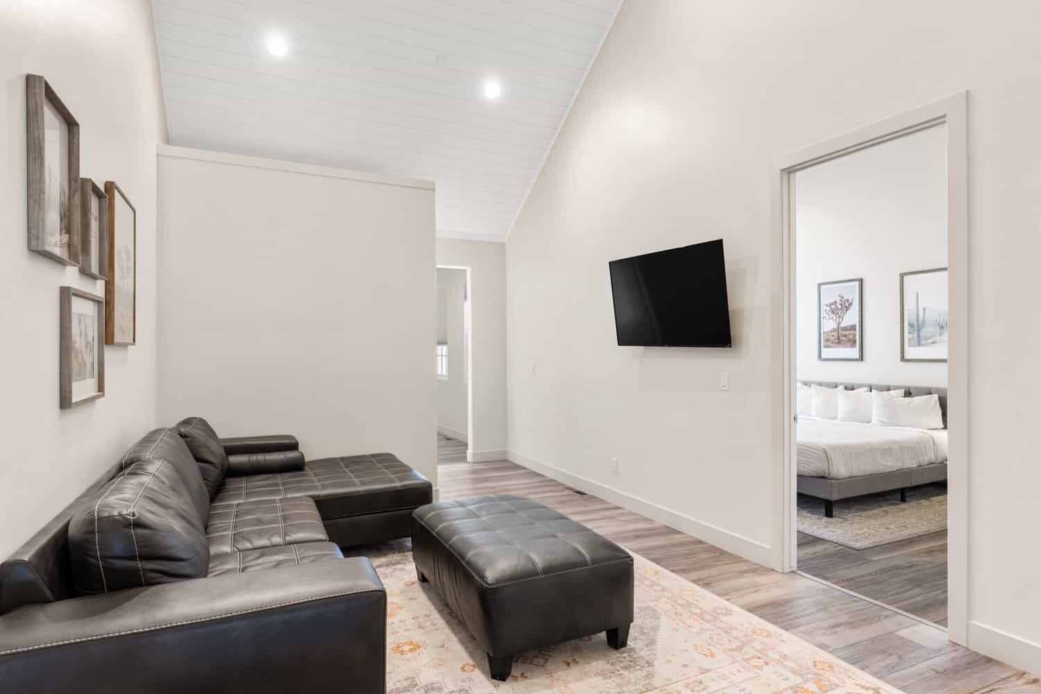 A modern living room with a sectional sofa, a flat-screen TV, and a hallway leading to a bedroom.