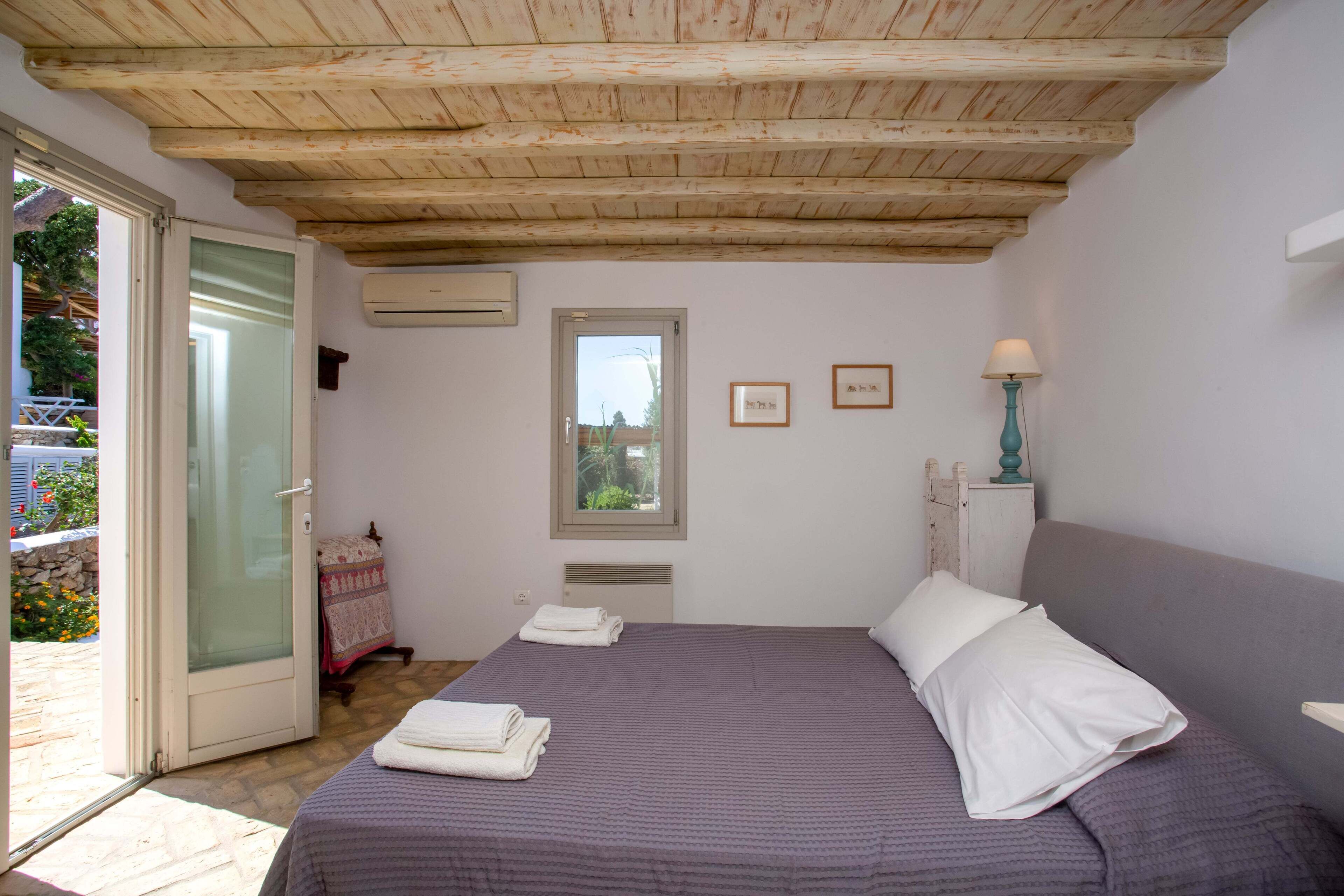 Un dormitorio con techo de madera, una cama con ropa de cama blanca, una ventana y una lámpara.