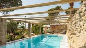 En swimmingpool med träpergola, stenmurar och utomhusmöbler.