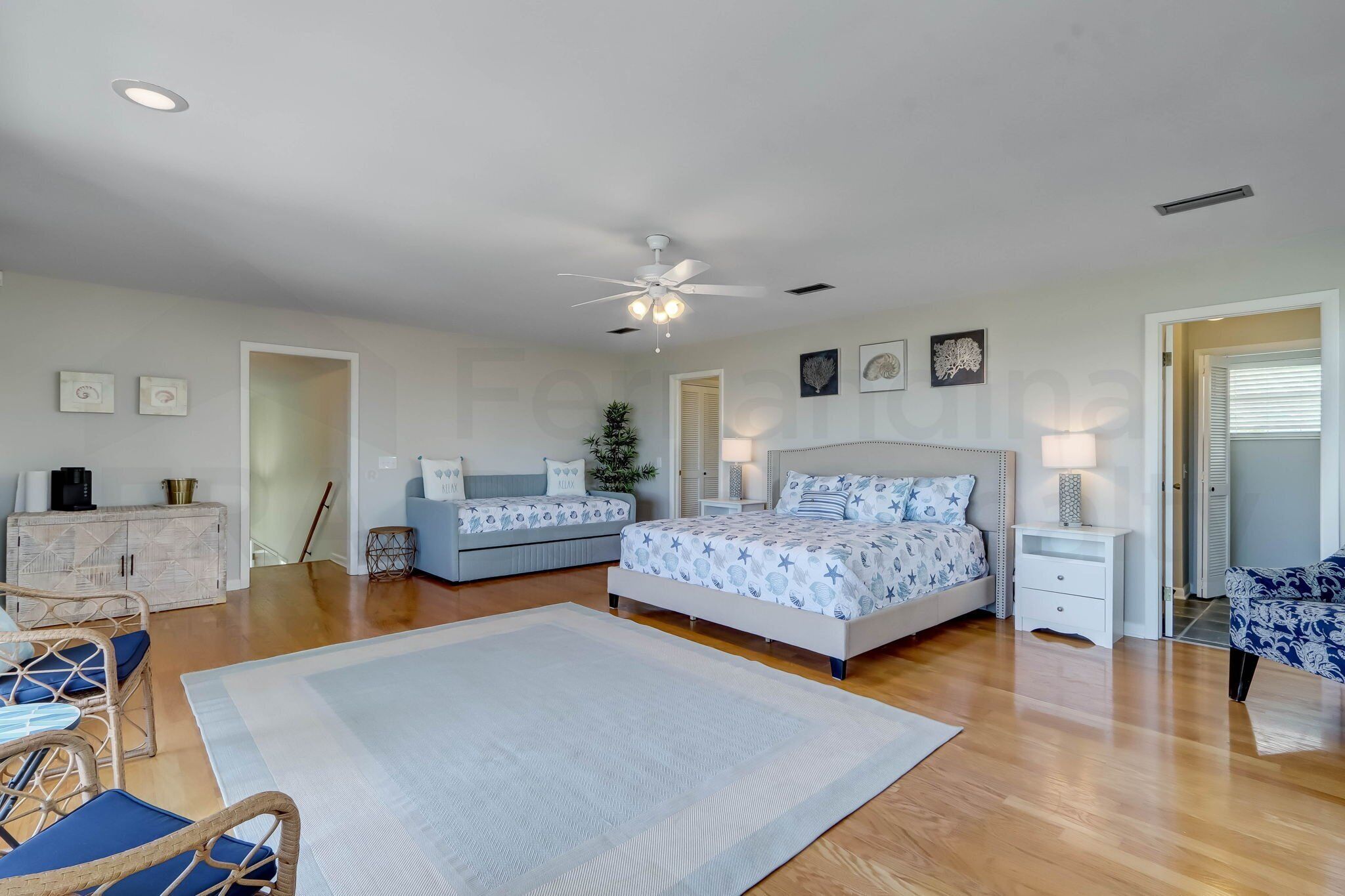 A bedroom with a large bed, two bedside tables, a ceiling fan, and a view of the outside.