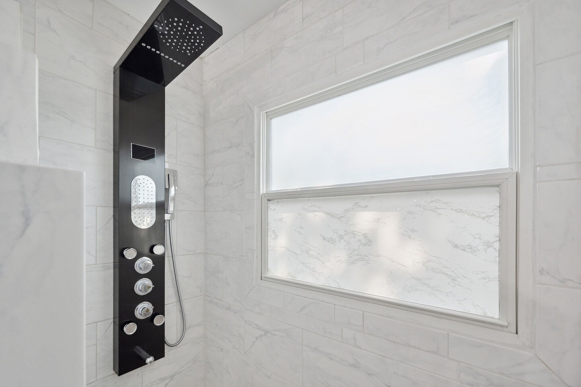A modern bathroom with a shower, a window, and marble tiles.