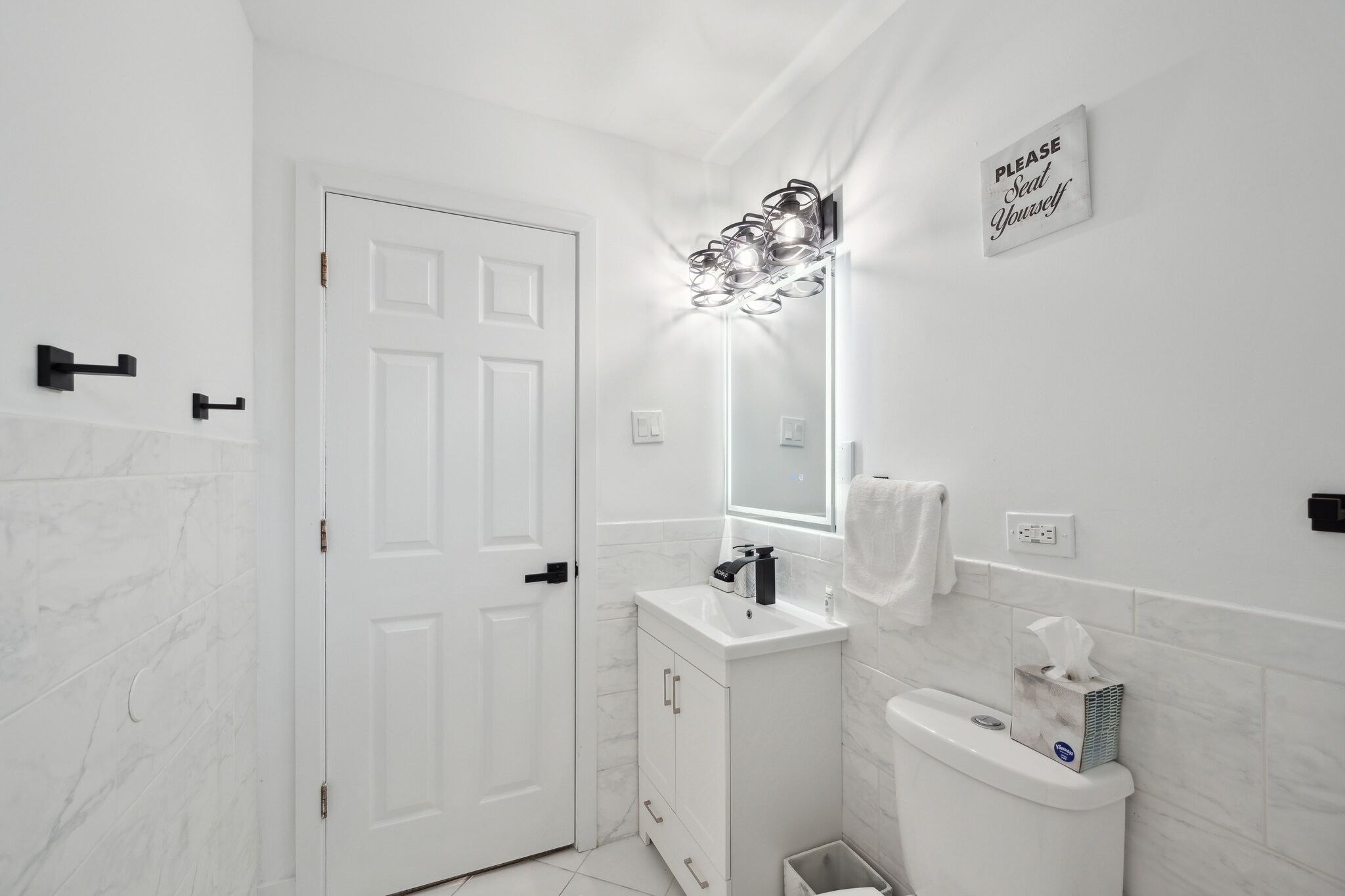 A modern bathroom with a white door, a vanity with a mirror, and a wall-mounted light fixture.