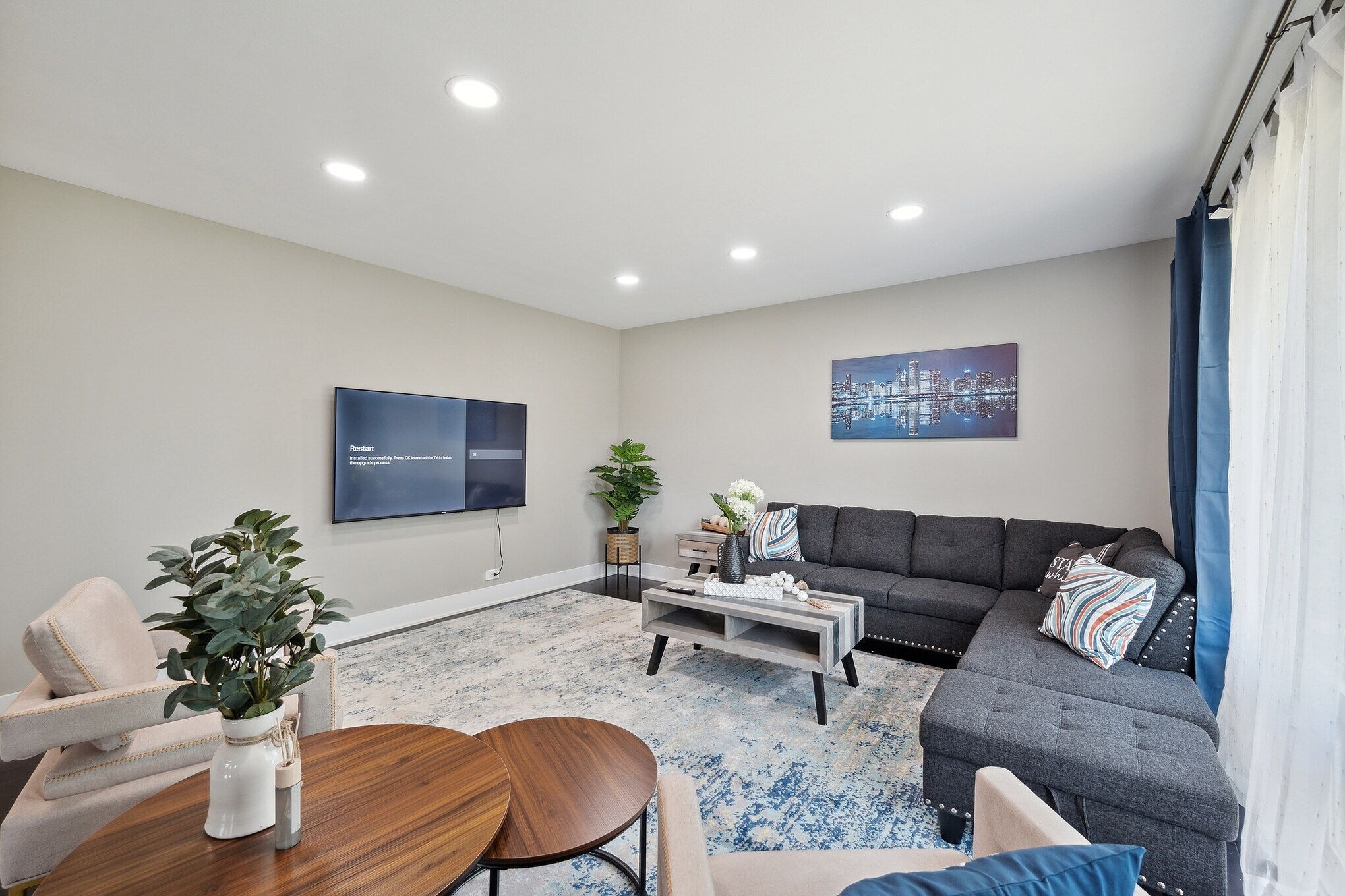 A modern living room with a grey sofa, a coffee table, a TV, and a cityscape painting.
