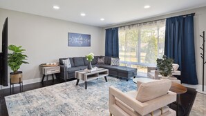A modern living room with a sectional sofa, a coffee table, and a large window with curtains. - Charming Contemporary Family Home 3 Bedroom Home by RedAwning (Glenview)