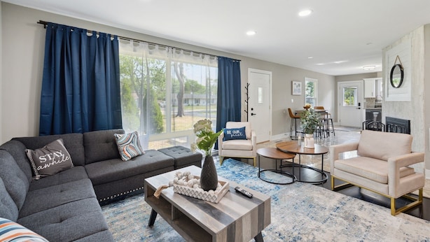 A modern living room with a sectional sofa, a coffee table, and a dining area with a table and chairs. - Charming Contemporary Family Home 3 Bedroom Home by RedAwning (Glenview)