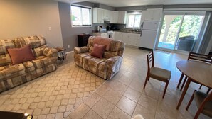 A living room with a sofa and chairs, a dining table, and a kitchen with cabinets and a refrigerator.