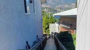 A wooden deck leading to a building with a white exterior, a window, and a view of a mountainous landscape.
