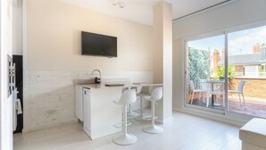 A modern kitchen with a TV, white bar stools, and a large sliding glass door to a balcony. - Penthouse With Private Terrace (Barcelona)