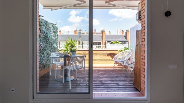 A sliding glass door leading to an outdoor patio with a table and chairs, a potted plant, and a brick wall. - Penthouse With Private Terrace (Barcelona)