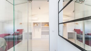 A modern hotel room with a glass partition, a bed with red and grey bedding, and a white wardrobe with hanging items. - Penthouse With Private Terrace (Barcelona)