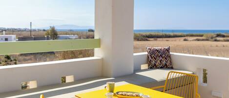 Una mesa amarilla con dos tazas y un plato de galletas en un balcón con vista al mar y a la costa.