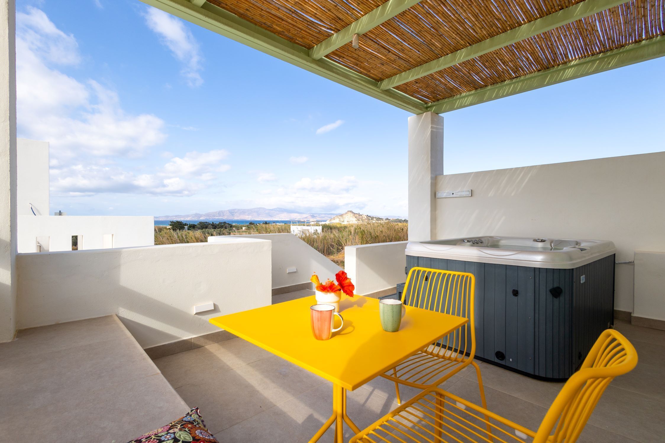Un balcon avec une table jaune, deux chaises jaunes, un jacuzzi et une vue panoramique.