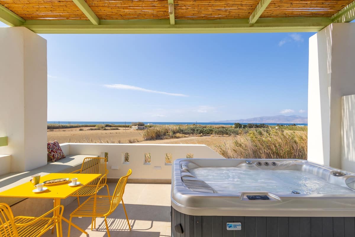 Un patio con un jacuzzi, sillas amarillas y una mesa con tazas y un plato.