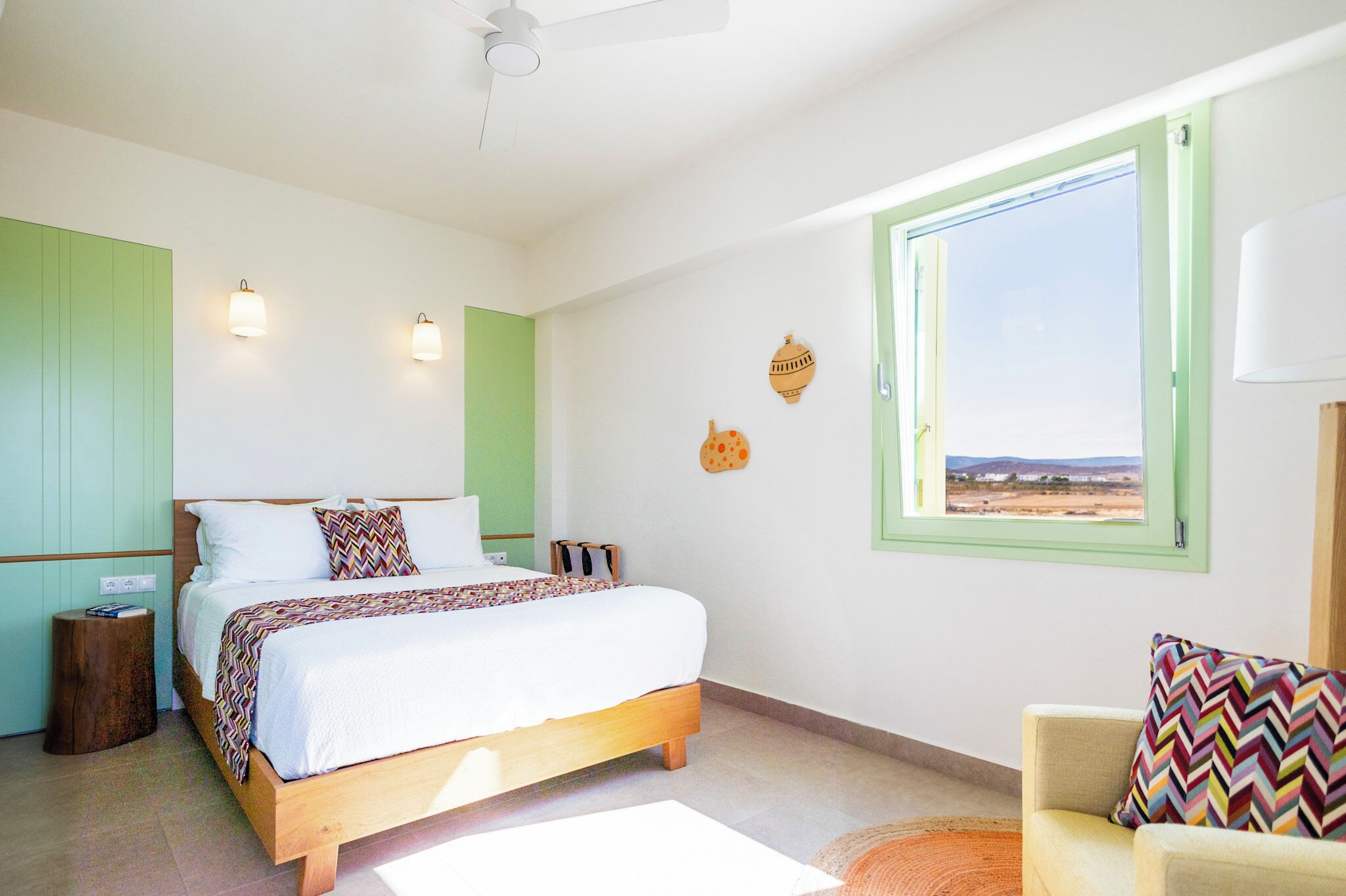 Un dormitorio con cama, una silla, una ventana con vistas e iluminación en la pared.