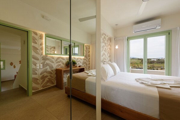 A modern bedroom with a large bed, a bedside table, a mirror, and a view of the countryside through a large window.
