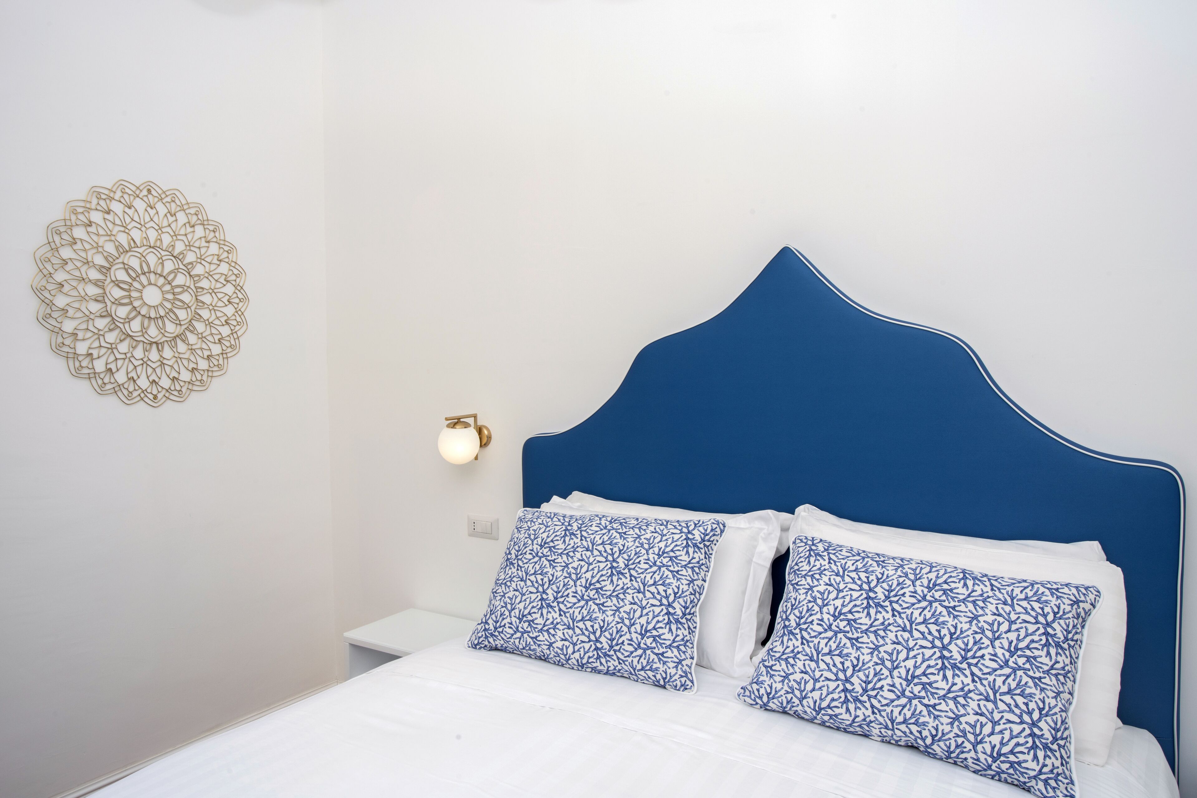 Una cama con cabecera azul, ropa de cama blanca y almohadas con estampado azul.