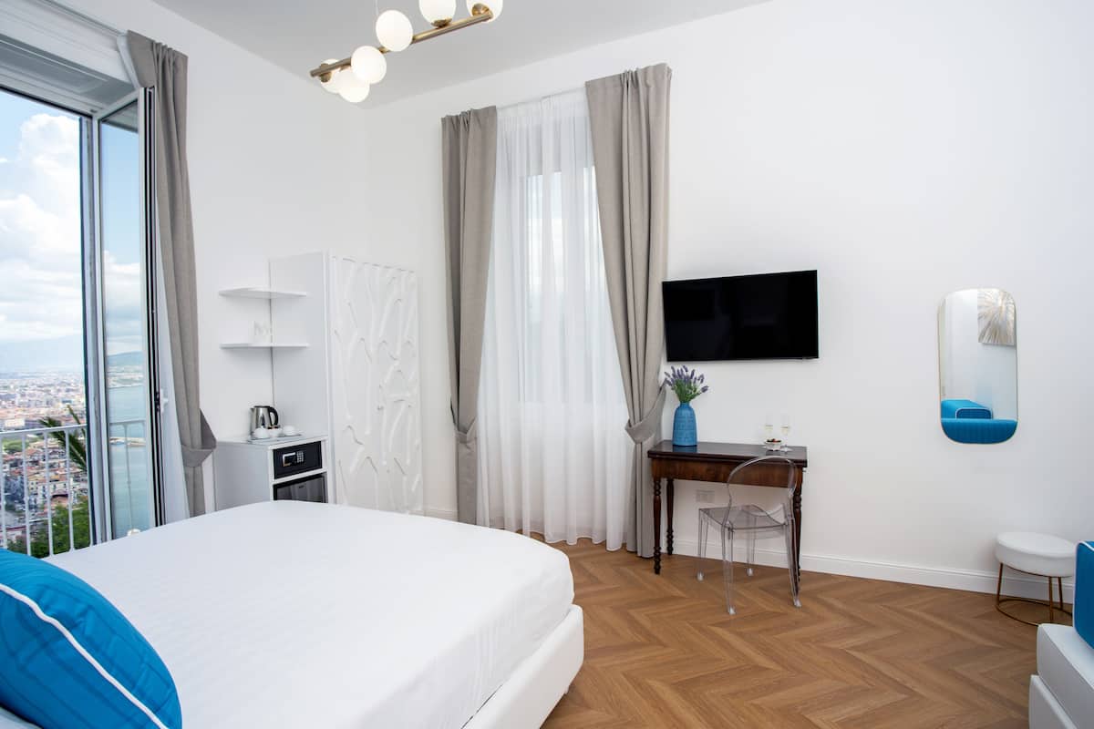 A modern hotel room with a large bed, a desk with a chair, a television, and a view of the city.
