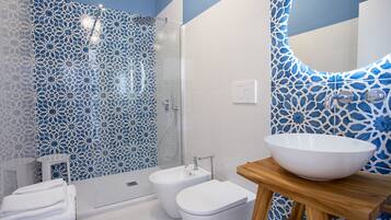 A bathroom with a shower, bidet, and a large sink on a wooden stool.