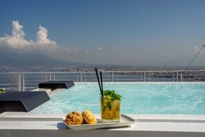 A poolside setting with a drink and snacks, overlooking a city and a bridge. - Relais al Castello (Castellammare di Stabia)