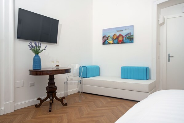 A modern room with a white sofa, a blue vase, a painting, and a TV on the wall. - Relais al Castello (Castellammare di Stabia)
