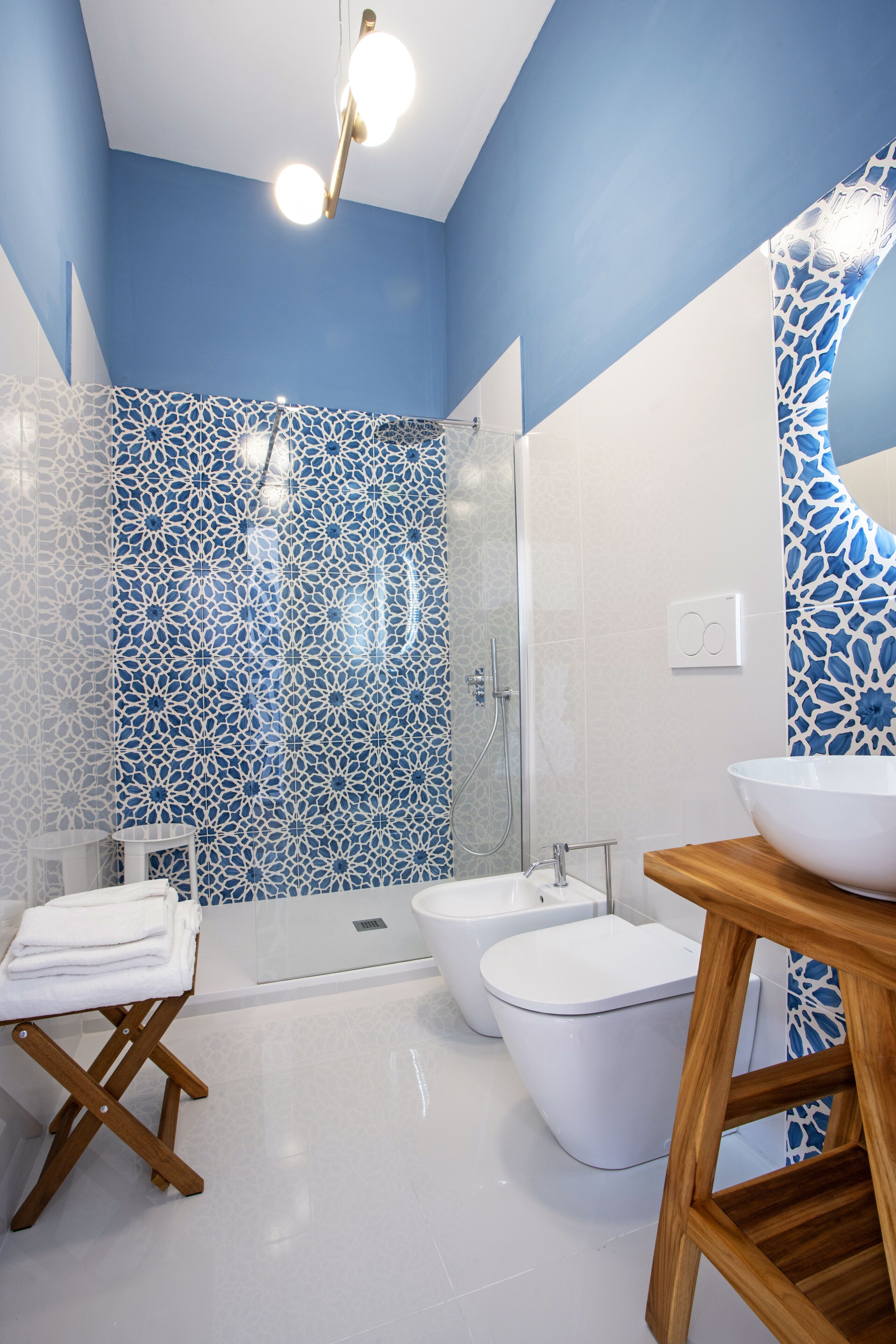 Un baño moderno con un diseño de azulejos azul y blanco, un mueble de tocador de madera, un lavabo blanco y una mampara de ducha de vidrio.