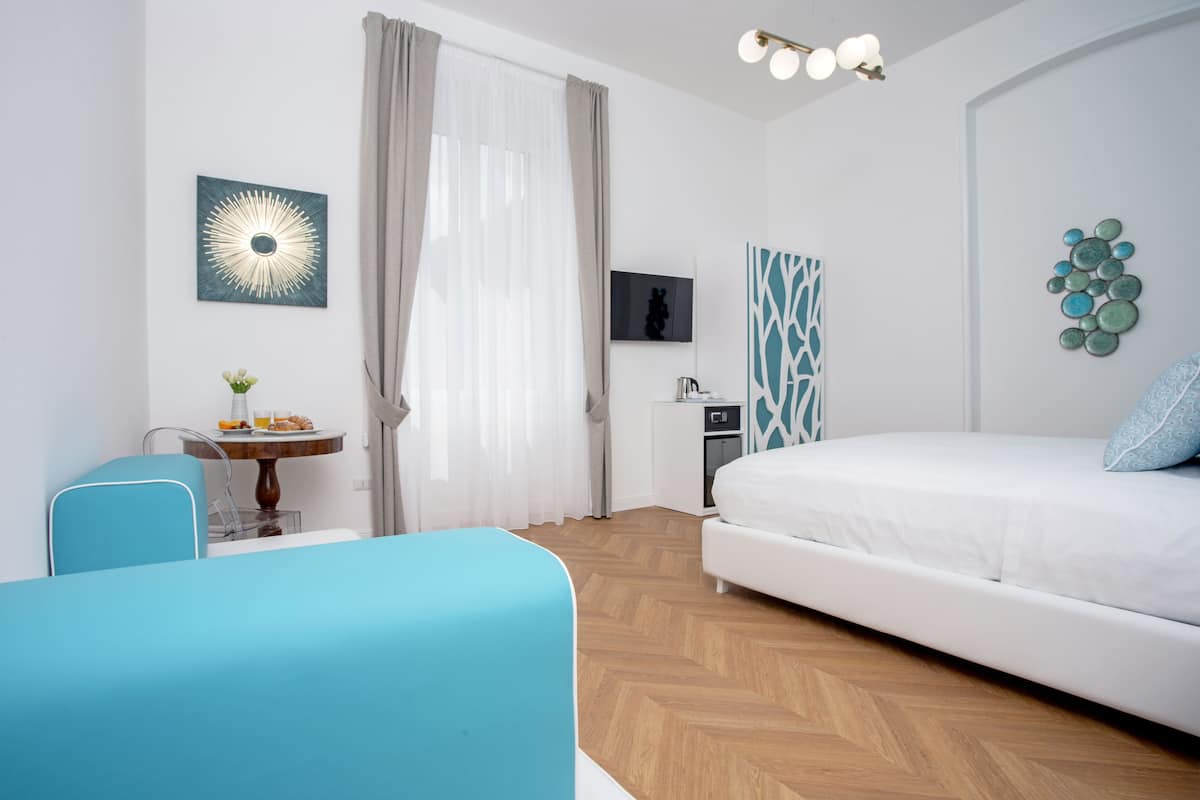 A modern hotel room with a bed, a desk, a chair, and a small table with breakfast items.