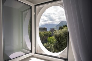 Habitación con un amplio ventanal circular que ofrece vistas a un paisaje montañoso y vegetación.