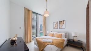 A modern hotel room with a large bed, a desk, and a view of a cityscape through a large window. - EDEN'S Homes & Villas - LIV Residence (Dubai)