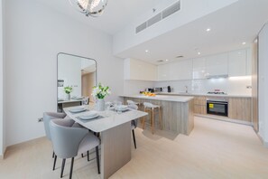 A modern kitchen with white cabinets, a central island, and a dining area with grey chairs and a white table.