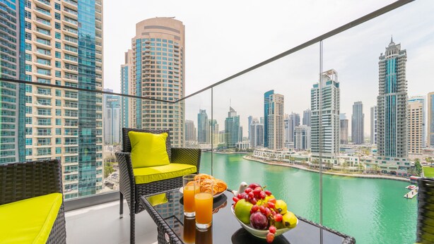 A balcony with wicker furniture, a glass table, and a bowl of fruit and juice. - EDEN'S Homes & Villas - LIV Residence (Dubai)