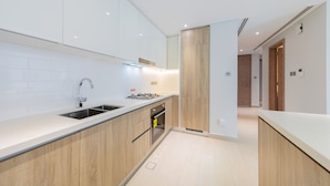 A modern kitchen with white cabinets, a stainless steel sink, and a built-in oven. - EDEN'S Homes & Villas - LIV Residence (Dubai)
