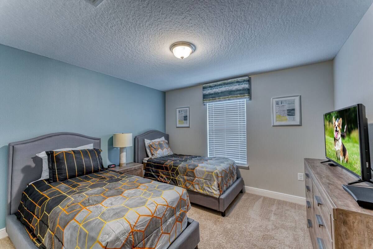 A bedroom with two beds, a TV, and a window with blinds.