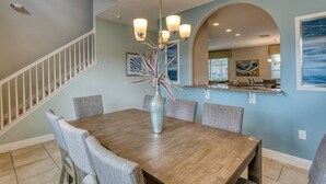 A dining area with a wooden table, grey upholstered chairs, a vase with plants, and a chandelier.