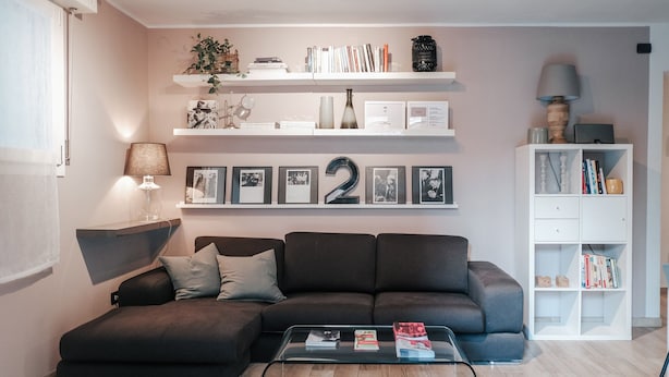 Ein modernes Wohnzimmer mit einem dunkelbraunen Ecksofa, einem Glastisch und einem Bücherregal mit Büchern und Dekoration.